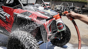 Person washing a red and black off-road vehicle with a renegade products hose foam gun