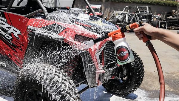 Person washing a red and black off-road vehicle with a renegade products hose foam gun
