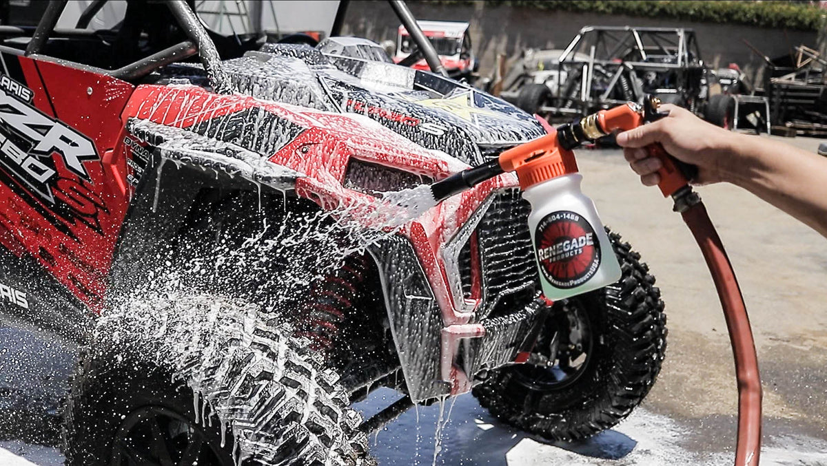 Person washing a red and black off-road vehicle with a renegade products hose foam gun
